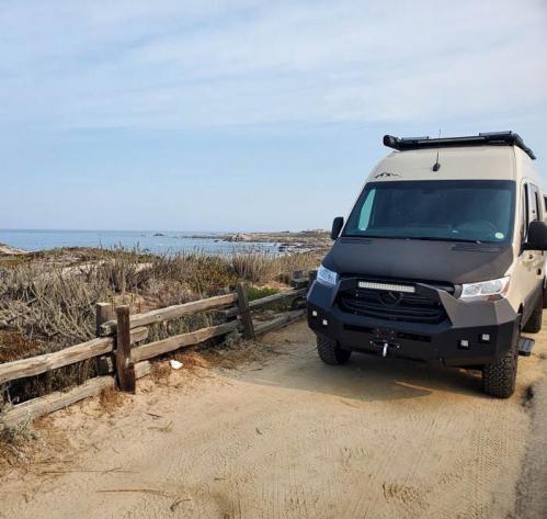 An Antero Adventure Van driving on a dirt road with a beach in the background